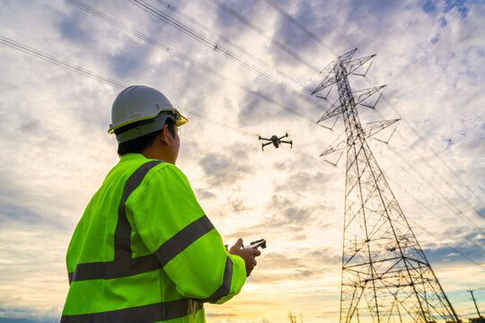 Asian engineer location use drone to fly inspections at the electric power station to view the planning work by producing electricity high voltage electric transmission tower at sunset.