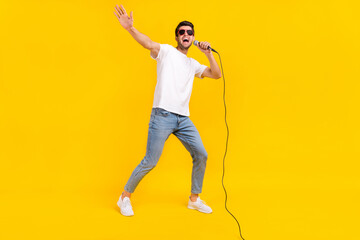 Fototapeta na wymiar Full length photo of nice millennial brunet guy sing wear eyewear t-shirt jeans sneakers isolated on yellow background