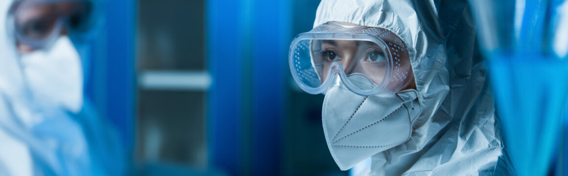 woman in goggles and medical mask near blurred scientist in laboratory, banner.