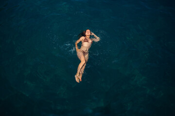 A beautiful young attractive woman in a swimsuit lies on the surface of the water at the sea. View from above. She is enjoying her vacation. Selective focus