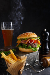Burger classique chaud sur une boite métallique  avec une bière et frites. 