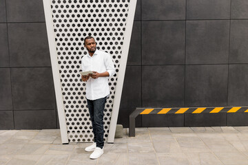 Confident serious businessman hold tablet, standing near the office, lost in thoughts about new startup. Stylish african american male employee in formal outfit looking at side, posing for the photo