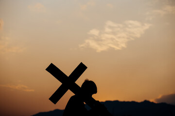 Silhouette of a man carrying a cross at sunset. concept of religion.