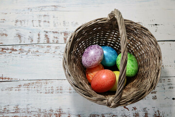 colorful easter eggs in a wooden wicker basket on a wooden table