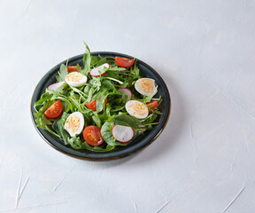 Salad with cherry tomatoes, fresh arugula and quail egg. Concept for a tasty and healthy meal. Vitamins in vegetables and herbs for immunity against the virus. Top view. Copy space