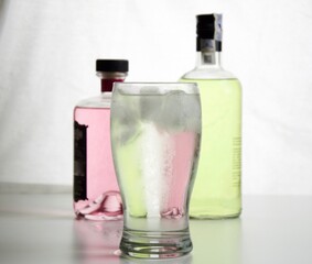 Glass with backlit gin and tonic and gin bottles in the background