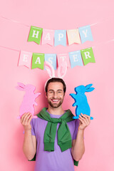 Photo of good mood handsome cute man celebrate easter hold two little bunny figurines isolated on pink color background