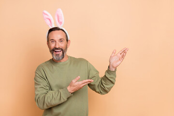 Portrait of attractive playful cheerful man wearing ears demonstrating copy space isolated over beige pastel color background