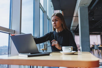 Portrait of a European young and successful woman sitting in a modern cafe with laptops. Pretty...