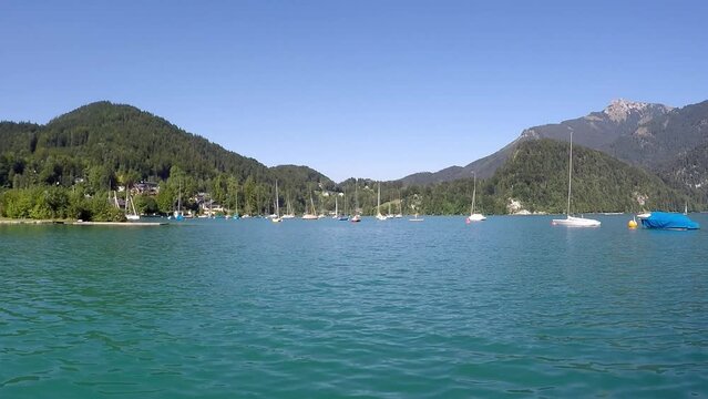 beautiful  blue lake in austria named wolfgangssee with mountains, smooth water, swaying sailboat near by a shipyard and a little village -a sunny day with a blue sky all in all a nice summeday