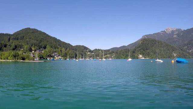 beautiful lake in austria named wolfgangssee with mountains, smooth water, swaying sailboat near by a shipyard and a little village -a sunny day with a blue sky all in all a georgous summer day