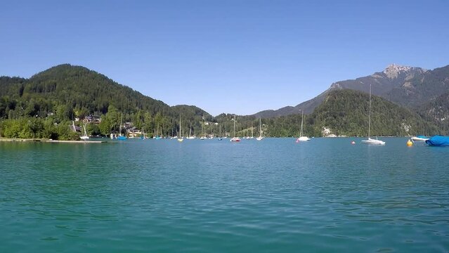 beautiful blue lake in austria named wolfgangssee with mountains, smooth water, swaying sailboat near by a shipyard and a little village -a sunny day with a blue sky all in all a georgous summer day