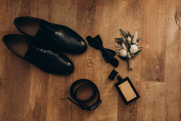 Wedding rings, perfume, shoes and belt. Male attributes on a wooden floor. selective focus