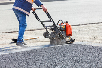 A road maintenance worker compacts asphalt with a petrol vibrating compactor.