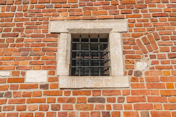 Window behind a wrought iron black metal grill on a red brick wall of a medieval building on a sunny day in Krakow