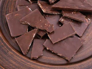 Pieces of broken chocolate bar on a brown plate.