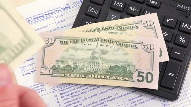 Men's hands throw several hundred dollar bills on the table with a calculator and a 1040 tax form. Tax payment, personal accounting, financial planning.