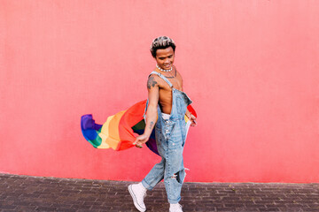 Happy guy in casuals walking against pink wall holding LGBT flag