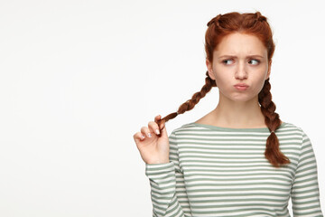 portrait of young ginger female standing over white studio background looks asied with sad and...