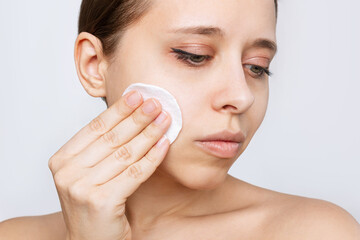 Close up of a young caucasian woman cleaning her face with cotton pad isolated on a white background. Skin care, cosmetology. Evening routine. The girl washes off her makeup with a cleanser. Close up
