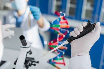 partial view of geneticist with micropipette near blurred microscope and dna model.