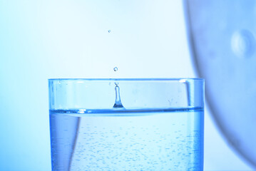 Pour water into a glass on a light blue background. Spraying water in glass. Water drops bounce in the glass.