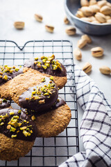 galletas de pistacho y chocolate sobre una rejilla, con un bol y pistachos desenfocados detr&aacute;s