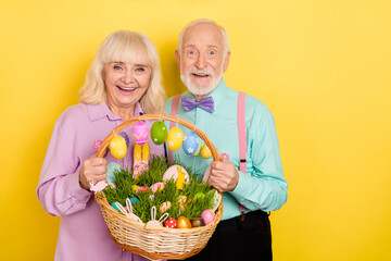 Portrait of two attractive cheery grey-haired spouses happy easter holding food isolated over bright yellow color background