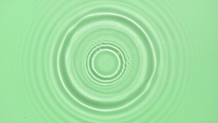 Drop falls down on water surface creating rings on green background | Beauty background shot for skin care cosmetics commercial
