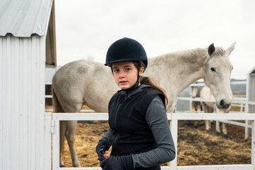 Girl with helmet and special clothes taking care of her horse before riding it.