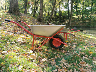 The garden wheelbarrow is empty in the park on an autumn day. Leaf collection, garbage collection, sand transportation. Seasonal landscaping.