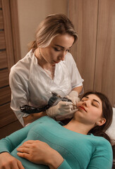 top view. beauty procedure. close up permanent tattoo. blonde female master in white medical gloves makes permanent eyebrow tattoo with smile on a brunette model girl. beauty concept, free space