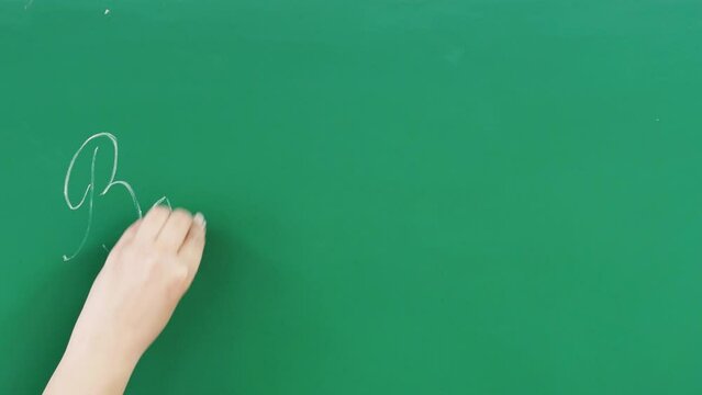 A woman's hand writes with white chalk on a green board the words Back to school and draws a cheerful emoticon. The concept of education, schooling, knowledge, study, learning process.
