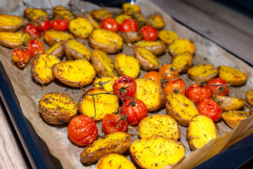 Baked potatoes and cherry tomatoes lying on a baking tray on the table..