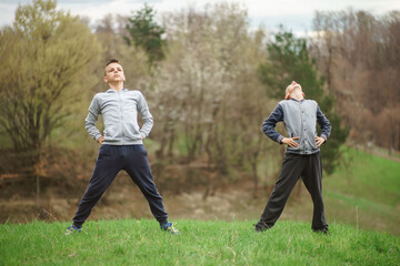 boys exercises outside, stretching his shoulder and back muscles