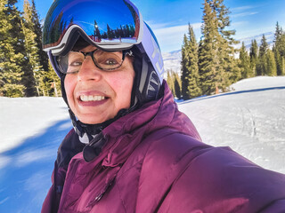 Selfie of smiling senior woman downhill skier with googles  on Colorado ski slope on sunny winter...