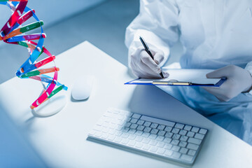 cropped view of scientist writing on clipboard near dna model and computer keyboard.
