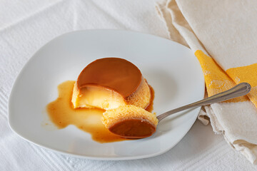 Single portion of creme caramel in a white plate and a teaspoon.