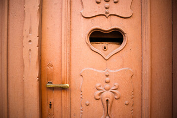 Beautiful antique terracotta door decorated with carvings and postal mail slot. Letter box in shape of heart with key hole. Valentine's day concept. Mailbox for love letters. Feeling love background.