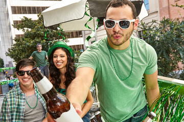 Happy man toasting friends wearing green hats and celebrating St Patrick's Day.
