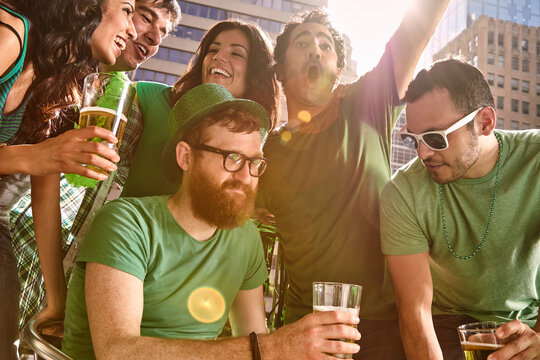 Friends all gathered around a table dancing and drinking beer at party on St Patrick's Day