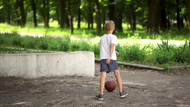 a boy in a white T-shirt in the park kicks a ball against the wall