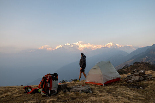 Hiker at sunrise standing at campsite looking off at mountains in distance. Nepal.