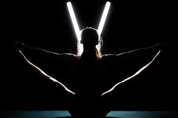 Fit woman practicing yoga poses. Silhouette girl doing exercise in studio against black background...