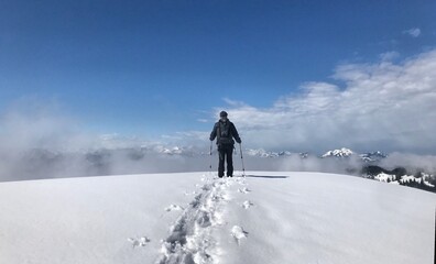 Bergwanderer (männlich) mit Rucksack und Stöcken von hinten im Winter mit Spuren im Schnee