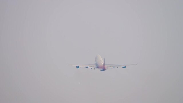 Jet four-engine airliner gaining altitude after takeoff, rear view in a long distance. Airport fence with barbed wire