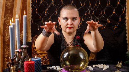 A bald woman fortuneteller tells fortune-telling on a crystal ball by candlelight in a saloon.