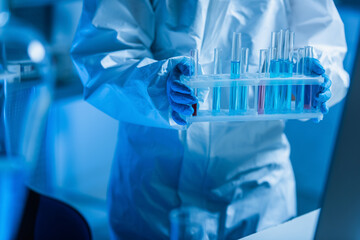 partial view of bioengineer in hazmat suit holding test tubes in lab.