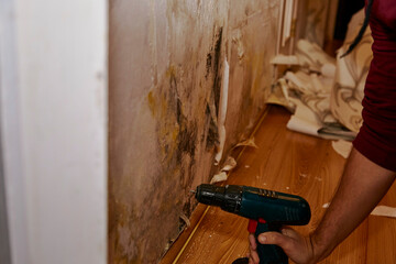 Removing the skirting board by drill before removing old wallpaper, cleaning and painting wall. Preparing for renovation of the flat. Close up. Truly moment
