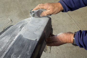Image of the hands of a body shop plastering and sanding the bumper of a car
